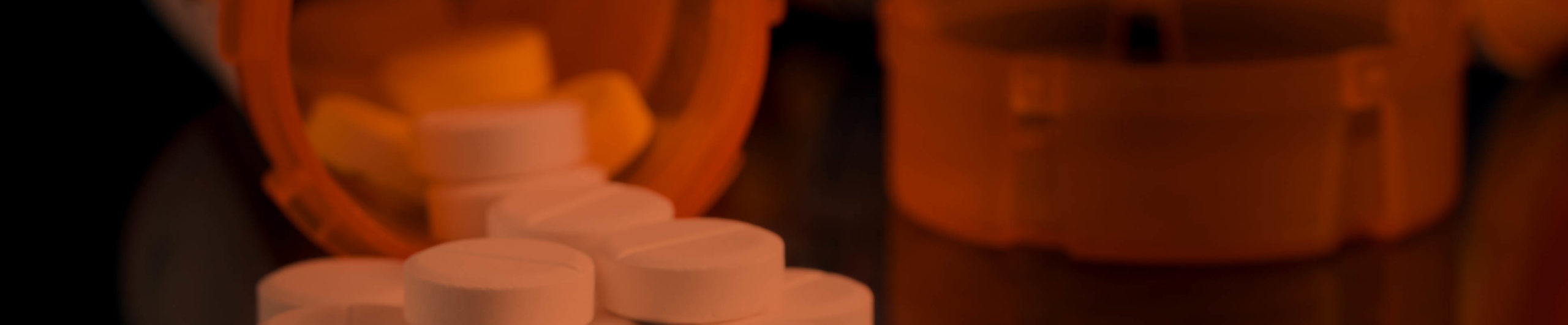 Macro of oxycodone opioid tablets with prescription bottles against dark background